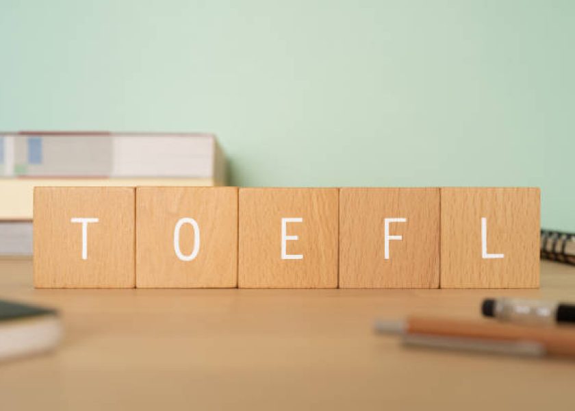 Wooden blocks with "TOEFL" text of concept, books, pens, and notebooks.