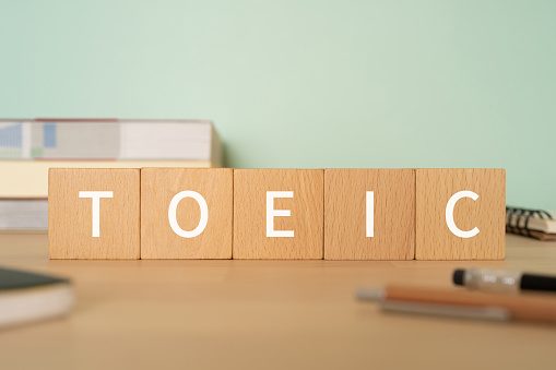 Wooden blocks with "TOEIC" text of concept, pens, notebooks, and books.